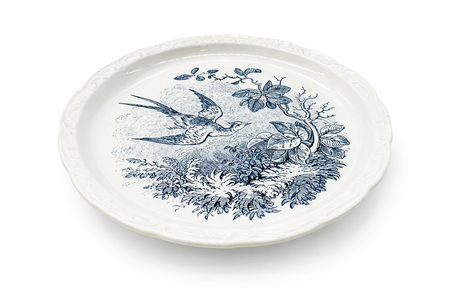 Assiette ancienne en faïence décor oiseau bleu, vue en perspective mettant en valeur le relief du bord mouluré et le décor central