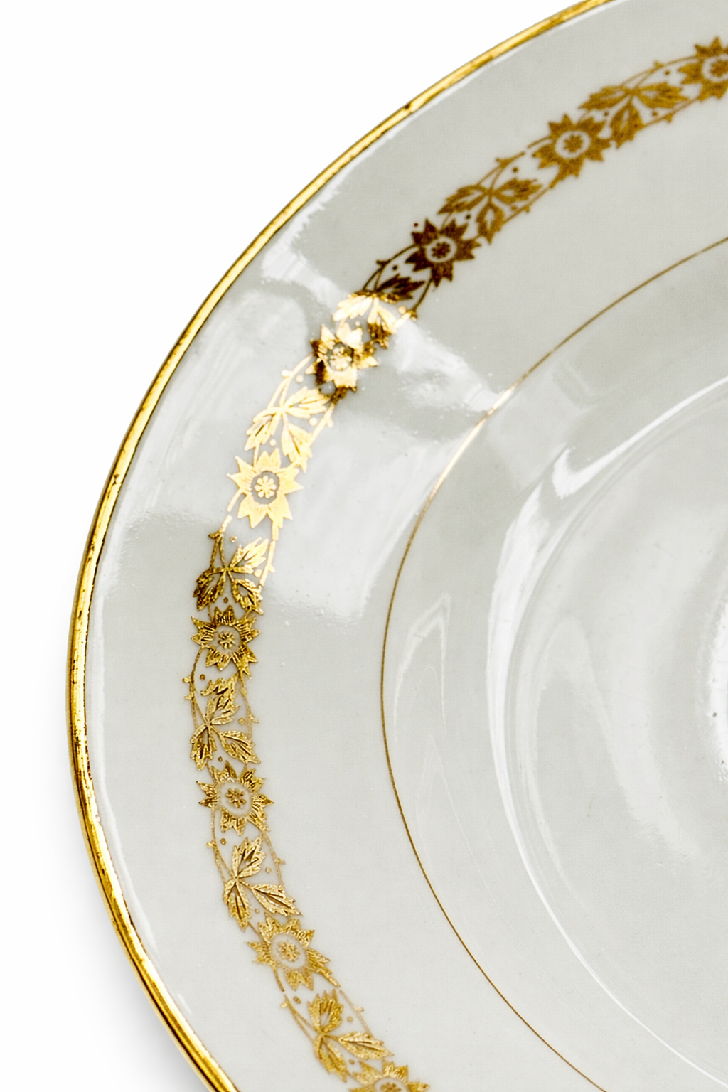 Détail de la frise florale dorée sur assiette en porcelaine blanche à liseré or