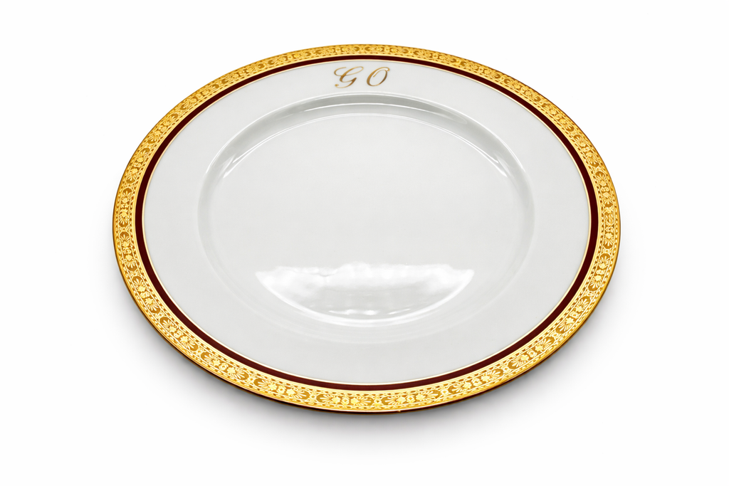 Assiette plate en porcelaine de Limoges vue en perspective, bordure dorée richement décorée et monogramme « GO »