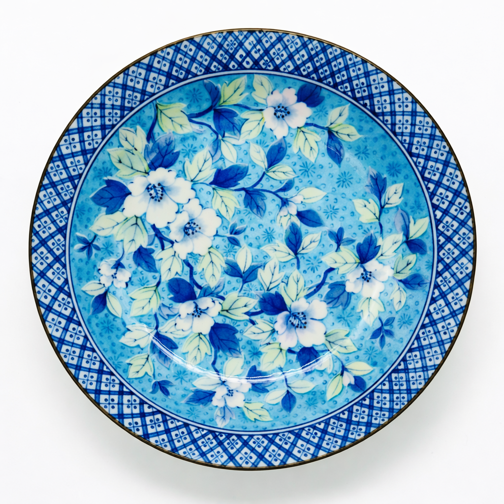 Assiette ancienne en porcelaine, décor floral bleu et blanc avec motifs de feuilles et fleurs stylisées, aile géométrique quadrillée, vue de dessus