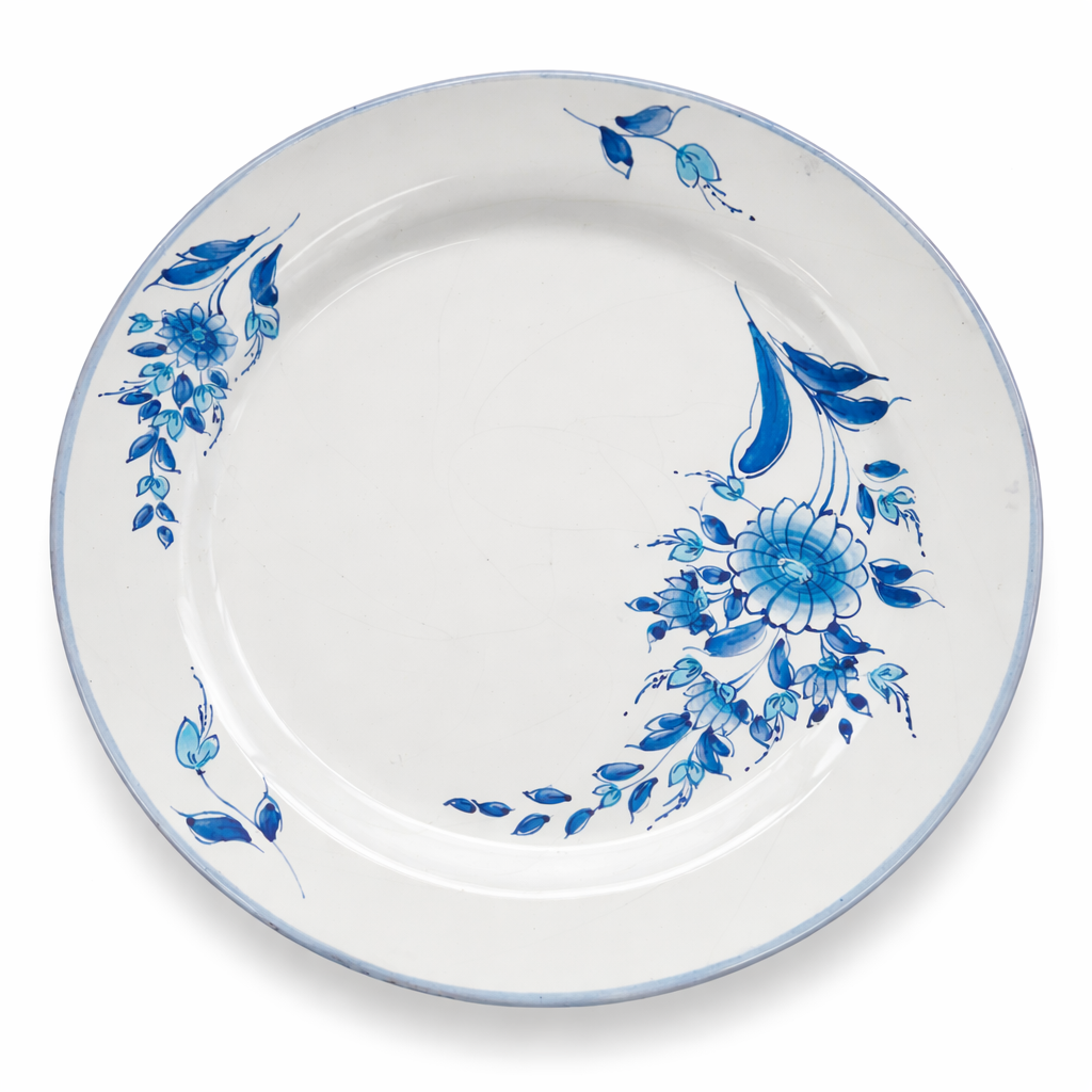 Assiette ancienne en céramique blanche à décor floral bleu peint, vue de dessus